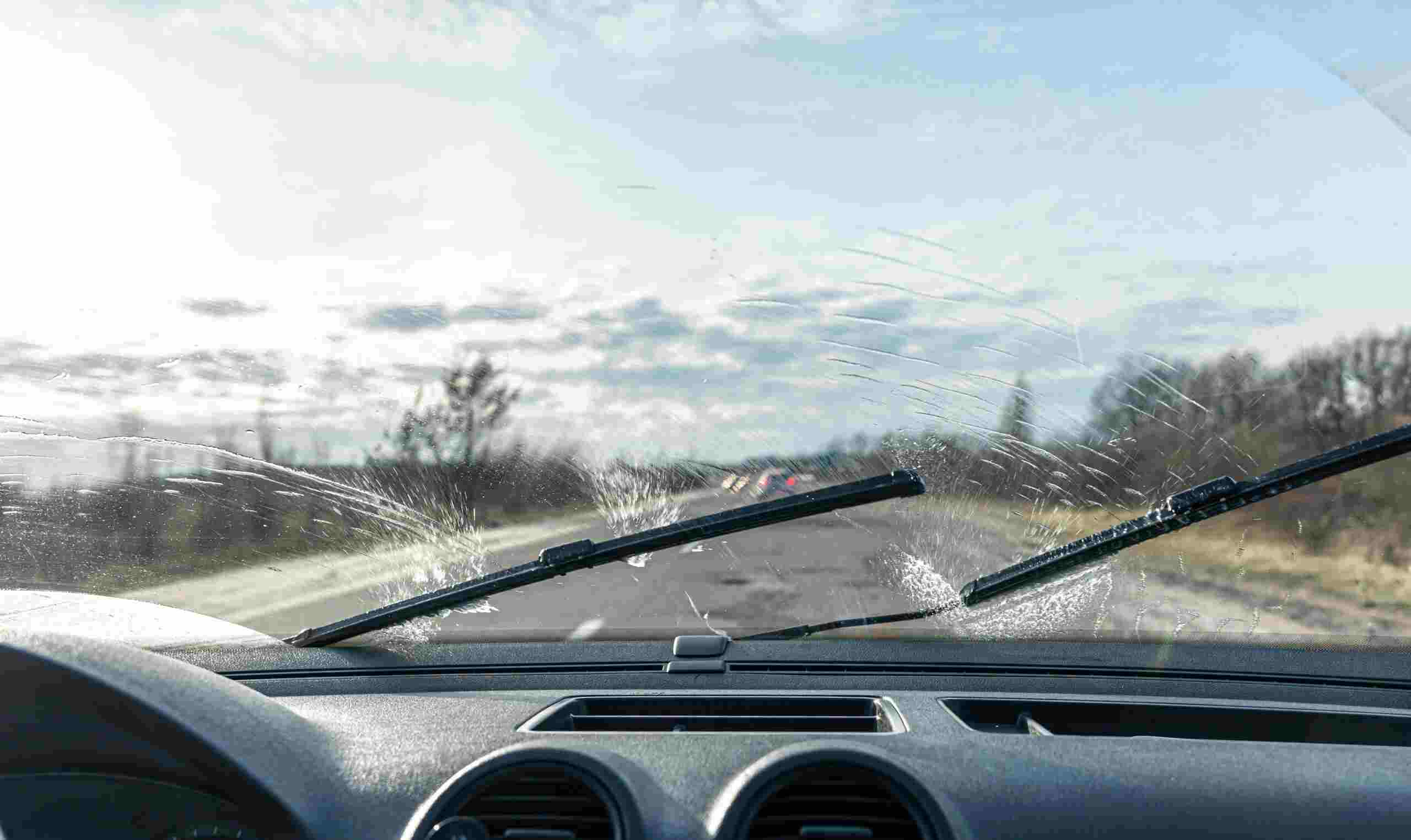 Car wipers clean windshields when driving in sunny weather, inside view.